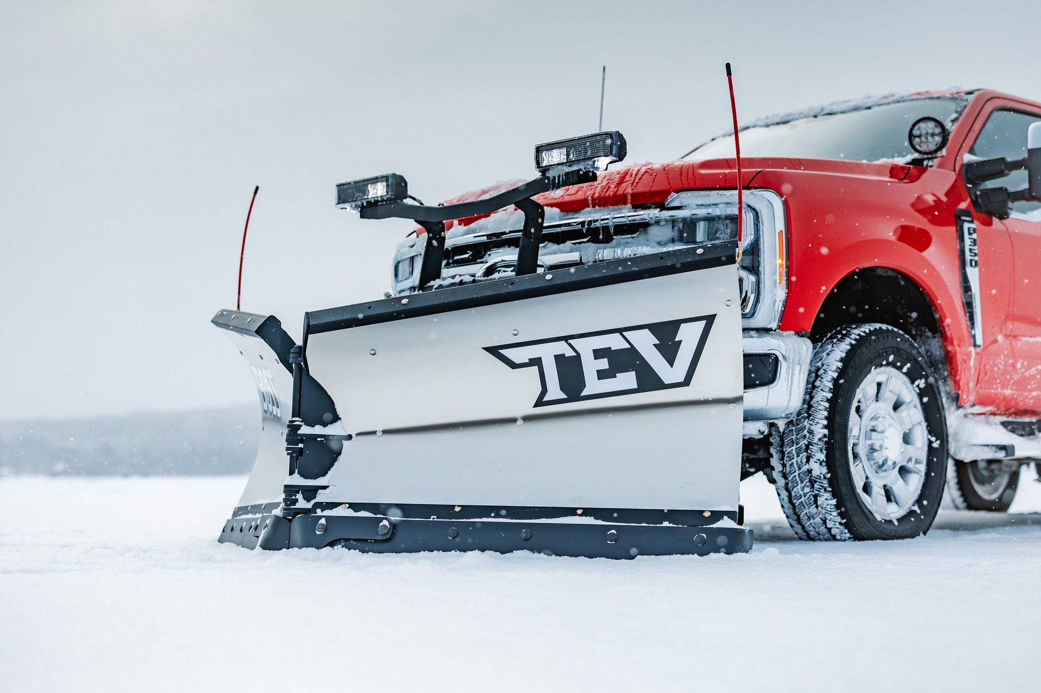 Red heavy duty truck equipped with TEV snow plow system in snowy conditions